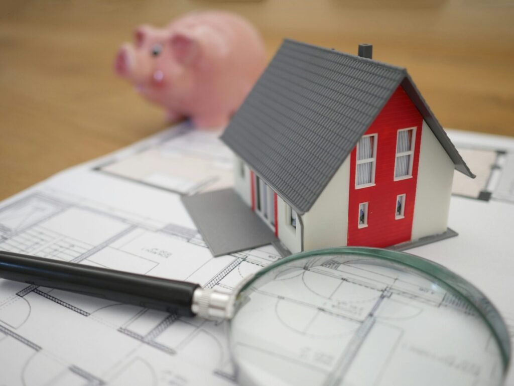 Évitez les erreurs lors de la demande de prêt immobilier Modèle de maison avec une loupe et une tirelire sur des plans de maison.