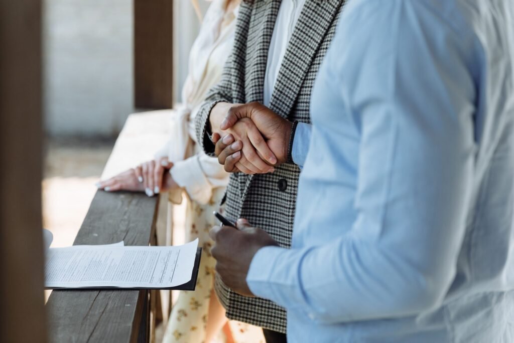 Poignée de main entre deux personnes au-dessus d'un contrat, illustrant un compromis de vente immobilier.