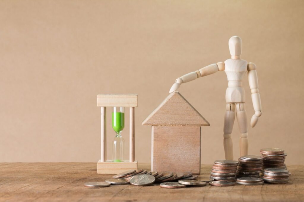 Maison miniature, pièces de monnaie et sablier illustrant le remboursement anticipé d’un prêt immobilier.