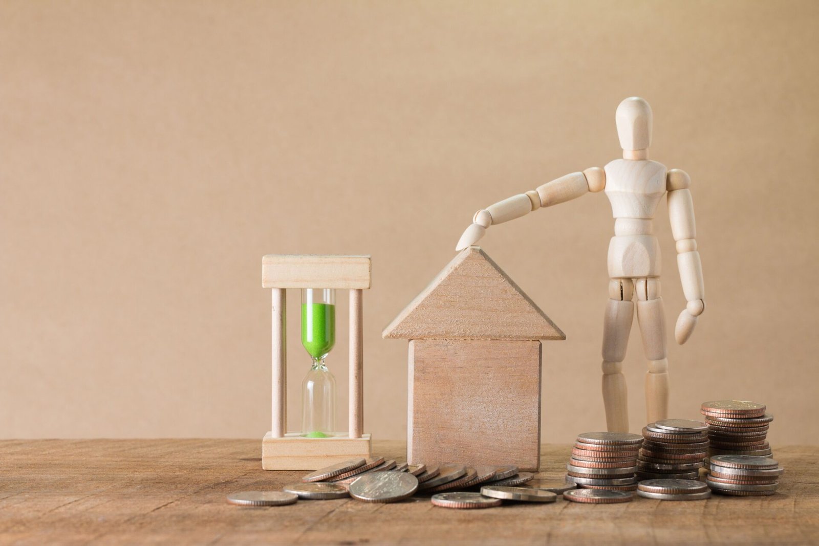 Maison miniature, pièces de monnaie et sablier illustrant le remboursement anticipé d’un prêt immobilier.